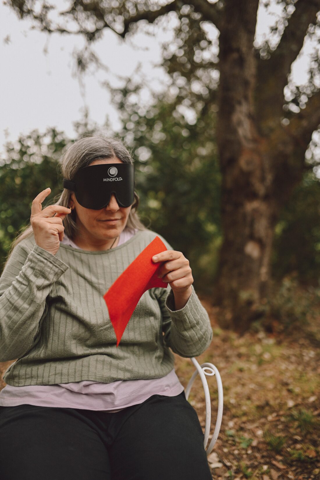 Persona con antifaz percibiendo con las manos una forma de fieltro rojo al aire libre.